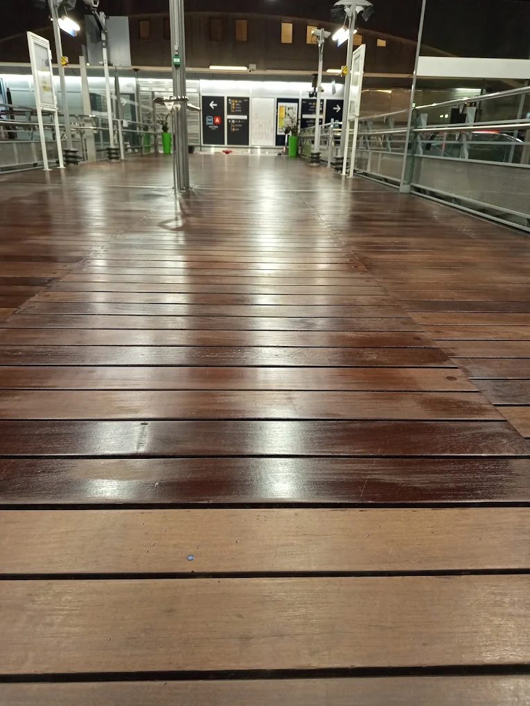 Passerelle en lames de bois nettoyée, encore humide, dans une gare aux abords éclairés
